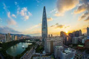この画像は、ソウルのシティスケープを捉えたもので、太陽が沈む夕刻の光に輝く高層ビルが印象的です。中央には目を引く尖った形の超高層ビルがそびえ立ち、周辺には様々な建物や川が広がっています。このように時代を象徴する近代的な景観と同じように、TikTokでZ世代を狙え！最新トレンドと企業の成功事例は、Z世代に響くトレンドをつかんで、企業が自社の魅力を伝えることができます。この画像が若い世代の目を惹くかのように、TikTokを活用したマーケティングは、Z世代に新鮮なインパクトを与える機会を提供します。